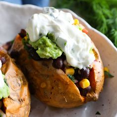 two stuffed sweet potatoes with black beans, guacamole and sour cream on top