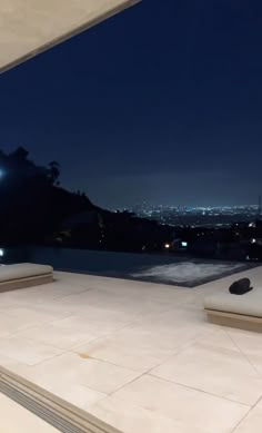 an outdoor lounge area at night overlooking the city lights in the distance, with two chaise lounges on the patio