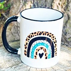 a white and black coffee mug with a heart on it sitting on a tree stump