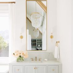 a white bathroom with a large mirror above the sink and flowers in front of it