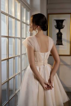 a woman in a white dress looking out the window