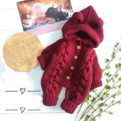 a baby's red sweater and cardigan next to a photo on a white table