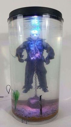 a glass jar with a figure in it on a white surface and a chain hanging from the bottom