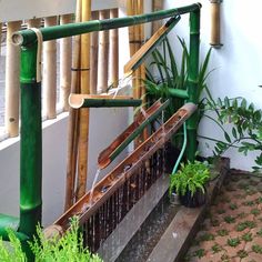 an outdoor water feature with bamboo poles and plants on the side of a building next to it