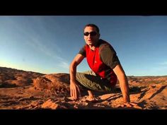 a man squatting on top of a rock in the desert