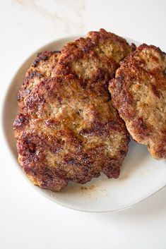 two hamburger patties on a white plate sitting on a counter top, ready to be eaten