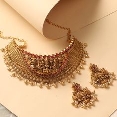 Description This statement choker necklace is an exclusive inclusion to our antique collection- traditional gold jewelry carved with Laxmi motifs and ivy design along with pearl & gold drop beads. Styled with simple yet gorgeous floral motifs and geometric patterns this is ideal for wedding events or festive occasions. Details & Specifications: Materials used : Brass Alloy with Antique Gold Plating Weight – Choker 180 gm, Earrings 45.86 gm Length – Choker 24.5 cm, Earrings 6.5 cm Make it custom Traditional Gold Jewelry, Antique Choker, Statement Choker, Statement Choker Necklace, Choker Set, Drop Beads, Floral Motifs, Geometric Patterns, Antique Collection