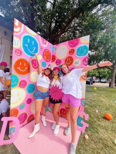 two girls standing in front of a giant sign with smiley faces on it's face