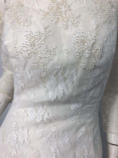 the back of a wedding dress with white lace and flowers on it's shoulders