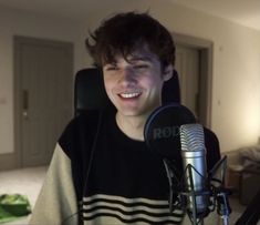 a young man smiling while sitting in front of a microphone and wearing a striped shirt