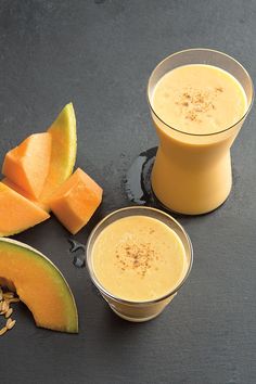 two glasses filled with orange juice next to sliced melon and pumpkin on a black surface