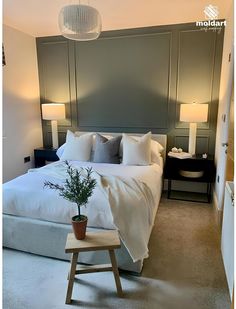 a white bed sitting next to two lamps and a table with a potted plant on it