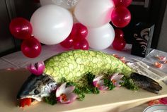 a fish that is laying on a cutting board with flowers and balloons in the background