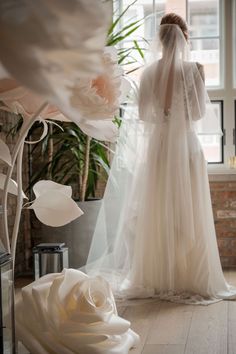 the back of a bride's wedding dress in front of a window with flowers