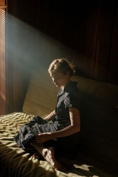 a woman sitting on top of a bed next to a window