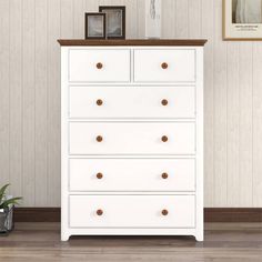 a white chest of drawers in a room with pictures on the wall and a potted plant next to it