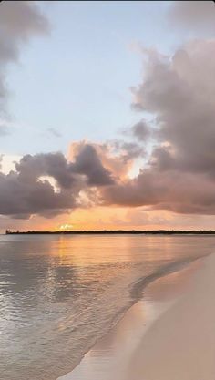 the sun is setting over the water at the beach with clouds in the sky above