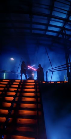 two people standing on top of a set of stairs with lights shining in the background