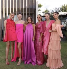 four women in dresses posing for a photo together on the lawn at an outdoor event