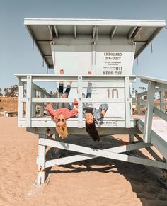 two people upside down in the sand under a lifeguards stand on their heads