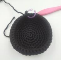 a black crochet bag with a pink handle on a white table next to a pair of scissors