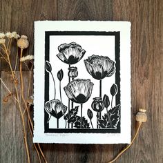 a black and white drawing of flowers on a wooden table next to some dried plants