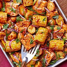 corn on the cob with potatoes and onions in a baking pan next to a fork