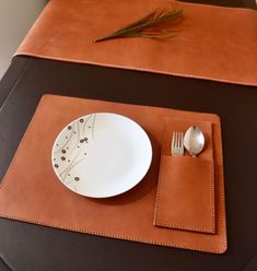 a place setting with silverware on a leather placemat and brown table cloths