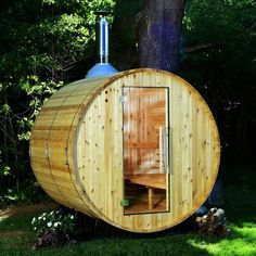 a wooden barrel sauna in the middle of a grassy area next to a tree