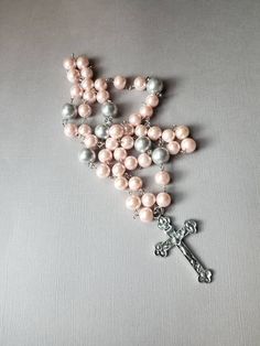 This Lutheran rosary has silver-toned findings and glass pearl beads in pink and gray. I used larger beads than I normally do on this one. It's really pretty. This rosary is hand-wired using silver-tone eye pins and my trusty little looper tool. The beads are connected by these loops. In the rosary itself, the small beads are 10mm pink glass pearls. The large beads are 12mm silver gray glass pearls. At the end of the stem is a silver-toned, budded metal crucifix. It measures 57mm x 35mm. 25.4 mm Silver Beaded Rosary For First Communion, Silver Pearl Rosary With 8mm Beads, Silver Pearl Rosary For First Communion, Handmade Silver Rosary With Crucifix, Silver Rosary With 8mm Beads And Crucifix, Handmade Pink Rosary With Cross Shape, Handmade Pink Rosary In Cross Shape, Handmade Pink Rosary With Cross, Handmade Pink Cross Rosary