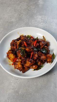 a white plate topped with meat and vegetables on top of a gray table next to a cup