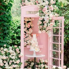 a pink phone booth decorated with flowers and greenery