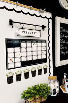 there is a black and white calendar on the wall next to some potted plants