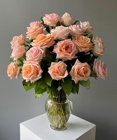 a glass vase filled with pink roses on top of a white table next to a gray wall