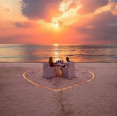 two people sitting at a table on the beach with sunset in the backgroud