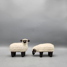 two ceramic sheep standing next to each other on a gray surface with clouds in the background