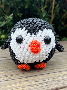 a small black and white penguin made out of plastic beads sitting on a wooden table