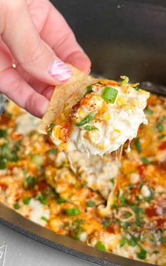 a hand holding a tortilla chip and scooping it into a casserole dish