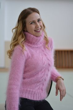 a woman sitting in a chair wearing a pink sweater and black pants with her hands on her hips