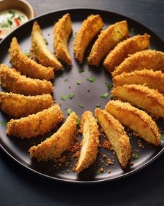 some fried food on a black plate with dipping sauce in the bowl next to it