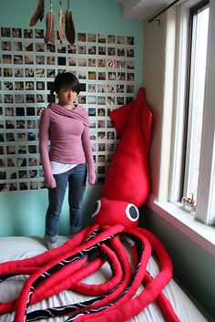 a woman standing next to a giant red octopus stuffed animal on top of a bed