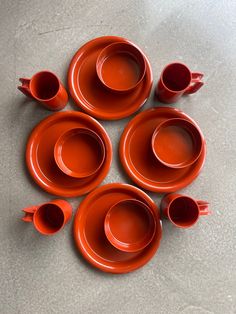 six orange cups and saucers are arranged in a circle on the floor, one is empty