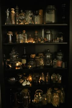 shelves filled with lots of glass jars and bottles on top of each other in a dark room