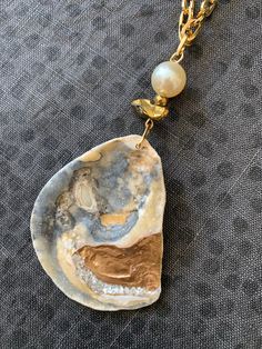 One of a kind handmade Oyster & Pearl Shell Necklace. An assemblage of pretty beads top this patterned oyster shell pendant: 12mm Pearl bead, faceted gold hematite bead and a chunky gold quartz nugget are all strung together on an 18K gold plated chunky paper clip style chain. The genuine oyster seashell has two unique sides: a beautiful natural pattern in grey, gold and white with a matte ribbed texture. The glossy reverse side is hand gilded with metallic gold paint and sparkling natural pearl Gold Abalone Shell Necklace In Unique Style, Unique Gold Abalone Shell Necklaces, Unique Gold Abalone Shell Necklace, Unique Gold Necklace With Abalone Shell, Gold Abalone Shell Pendant Jewelry, Artisan Gold Jewelry With Pearl Charm, Unique Handmade Gold Pearl Necklace, Unique Gold Jewelry With Abalone Shell, Elegant Gold Beaded Shell