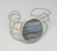 This is a 30 x 40mm blue lace agate cabochon set in .925 sterling silver (embellished bezel set) on a 3 wire cuff. approx. dimensions 5.50" around wrist 1.75" width at stone Silver Sterling Silver Cuff Bracelet With Cabochon, Handmade Oval Sterling Silver Cuff Bracelet, Adjustable Oval Agate Jewelry, Adjustable Oval Sterling Silver Cuff Bracelet, Adjustable Sterling Silver Cuff Bracelet With Cabochon, Adjustable Cabochon Sterling Silver Cuff Bracelet, Adjustable Sterling Silver Cabochon Cuff Bracelet, Silver Cabochon Cuff Bracelet Gift, Silver Agate Gemstone Cuff Bracelet