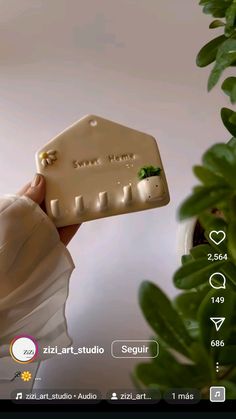 a person holding up a small white object in front of a plant with green leaves