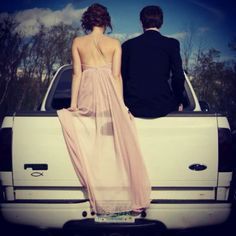 a man and woman sitting on the back of a white pickup truck looking at each other