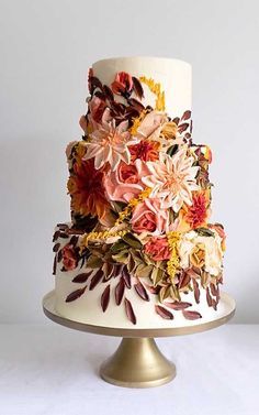 a three tiered cake decorated with flowers on a gold plated stand against a white background