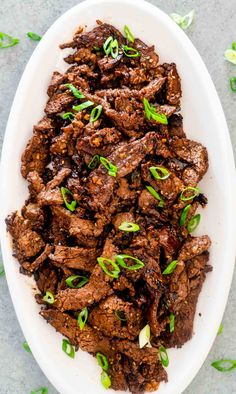 a white bowl filled with beef and green onions on top of a gray countertop