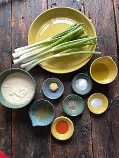 several bowls and spoons are arranged on a wooden table with green onions in them